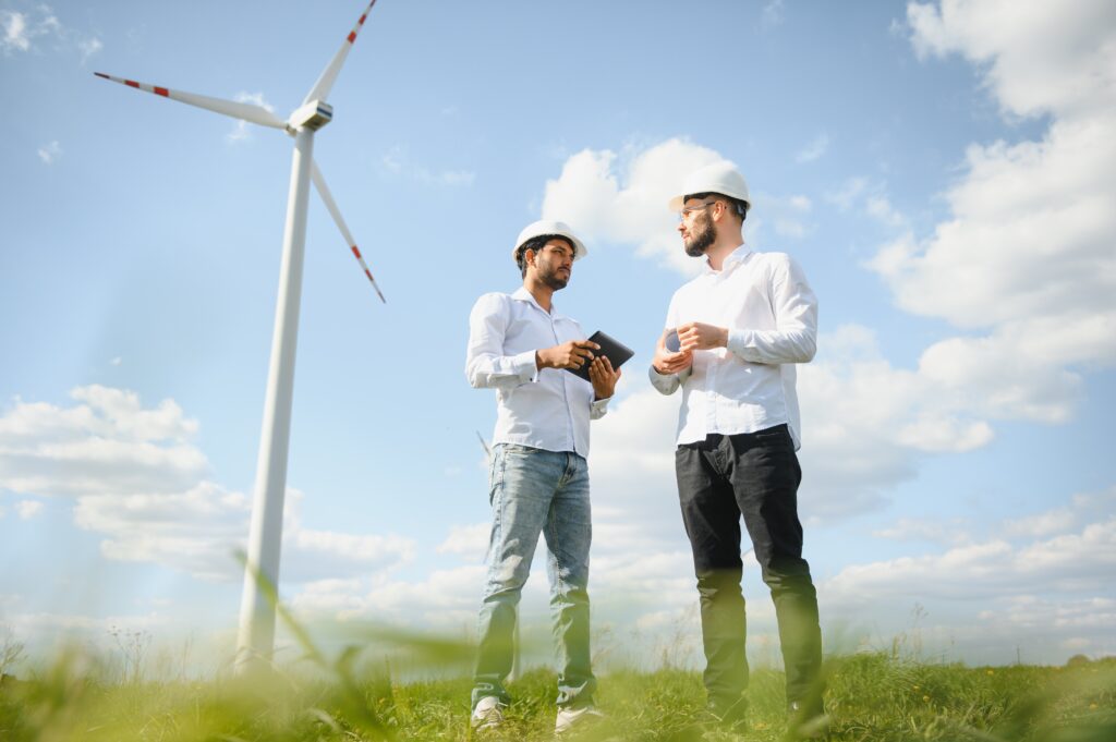 Two engineers discussing against turbines on wind turbine farm.