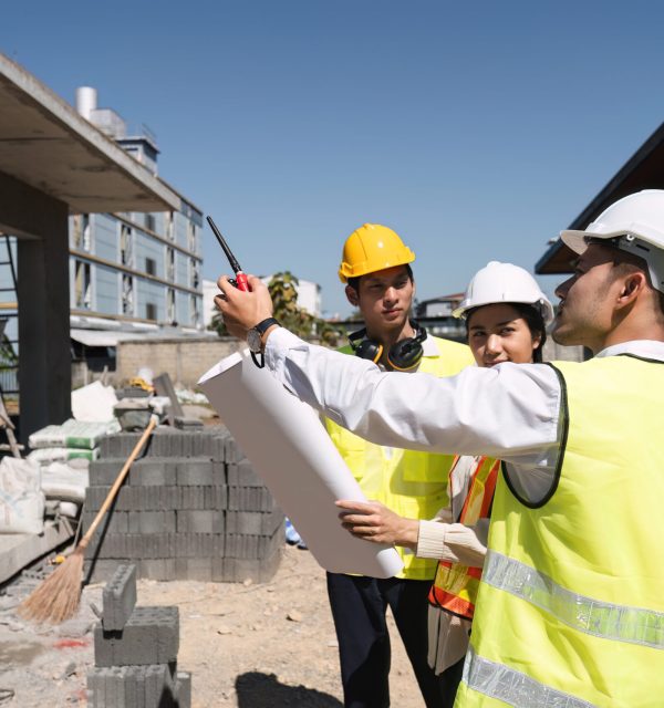 Team of professional civil engineers and architects holding project plan paper, supervising and controlling construction project work at construction site.